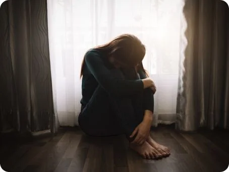 Cannabis bei Depressionen: Chancen, Risiken und wissenschaftliche Erkenntnisse Frau sitzt niedergeschlagen auf dem Boden vor einem Fenster und hält den Kopf gesenkt