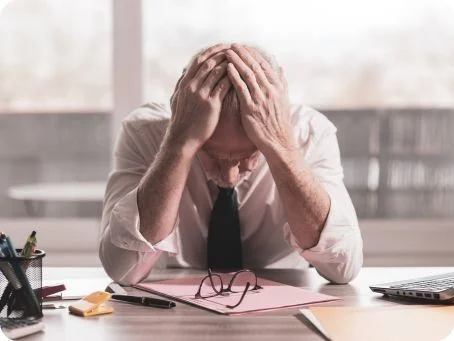 Einsatz von medizinischem Cannabis bei Stress und Burnout Mann sitzt erschöpft am Schreibtisch und hält den Kopf in den Händen