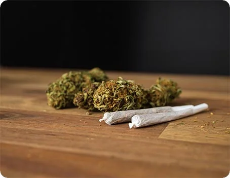 Zwei Joints neben getrockneten Cannabisblüten auf Holztisch