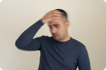 Mann hält sich aufgrund von Schwindel den Kopf, Gesicht ist verschwommen dargestellt